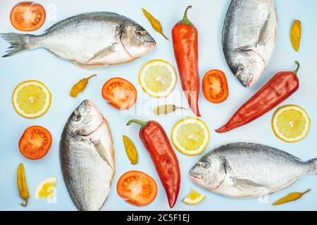 Dorado Fisch und Gemüse: Gurke, Tomaten, Pfeffer, Zitrone liegen auf blauem Hintergrund. Hintergrundtextur für die Küche Stockfoto