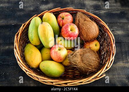 Früchte, Mango, Kokosnuss, Apfel in einem Korb auf schwarzem Holzgrund mischen Stockfoto