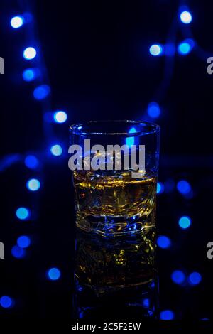 Ein Glas Whiskey auf den Felsen mit etwas Eis auf dem Tisch. Konzept der harten Alkohol. Mit festlichen Urlaub Bokeh Stockfoto