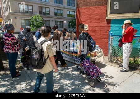 Die New Yorker holen am Donnerstag, den 25. Juni 2020, an einem Tisch des NYS-Vereinen Richard Gottfried im New Yorker Stadtteil Chelsea kostenlose Masken und Handdesinfektionsmittel ab. (© Richard B. Levine) Stockfoto