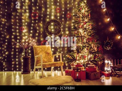 Traditionell eingerichtetes Wohnzimmer am Heiligabend. Viele Party Lichter beleuchtet, geschmückt Baum mit einem Vintage-Stuhl und viel rot und Gold. Stockfoto