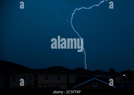 Heller Blitz im dunkelblauen Himmel über den Häusern, Gewitter. Stockfoto