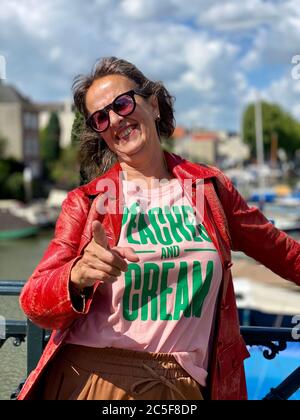 Porträt einer reifen älteren attraktiven Frau trägt Sonnenbrille und Vintage roten Lederjacke an einem Geländer lehnt, zeigt Emotion lächelnd. Stockfoto