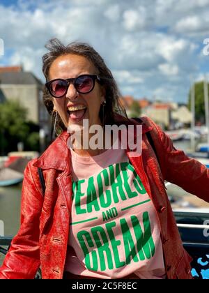 Porträt einer reifen älteren attraktiven Frau trägt Sonnenbrille und Vintage roten Lederjacke an einem Geländer lehnt, zeigt Emotion lächelnd. Stockfoto