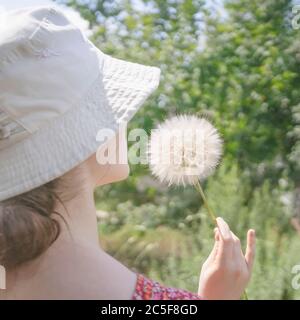 Löwenzahn in der Hand unwissbar Teenager-Mädchen in einem Hut, sonnigen Sommertag, Bauernhof, rustikale Natur, Urlaub, ländlichen Lebensstil Stockfoto