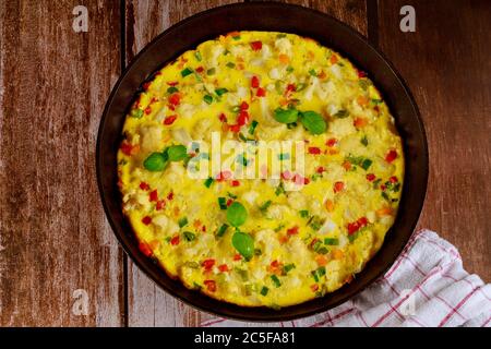 Hausgemachtes Omelett mit Gemüse in Pfanne auf Holzboden. Gesundes Lebensmittelkonzept. Stockfoto