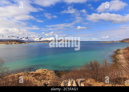 Türkisfarbenes Meer, hinter schneebedeckten Bergen der Insel Senja, Sommaroysund, Sommaroy, Troms, Norwegen Stockfoto