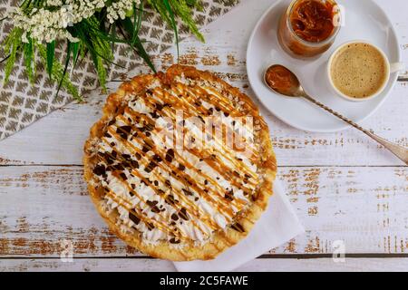 Köstliche Karamell-Schokoladencreme-Pie mit Tasse Kaffee auf weißem Holztisch. Stockfoto
