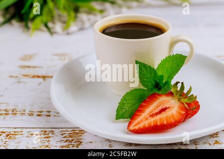 Tasse schwarzen Kaffee mit Schokolade und Erdbeere auf weißem Holztisch. Stockfoto