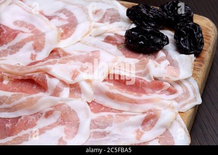 Speckscheiben mit Pflaumen auf Holzschneidebrett Stockfoto