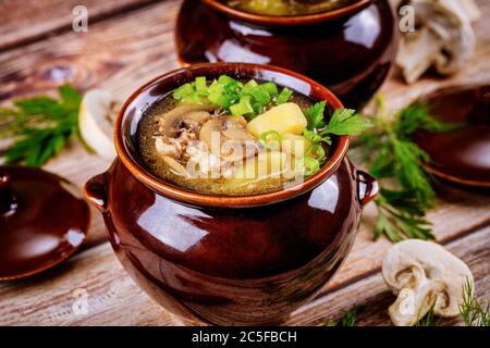 Kartoffel mit Pilzen und Fleisch in einem Tontopf mit Kräutern auf Holztisch geschmort.. Stockfoto