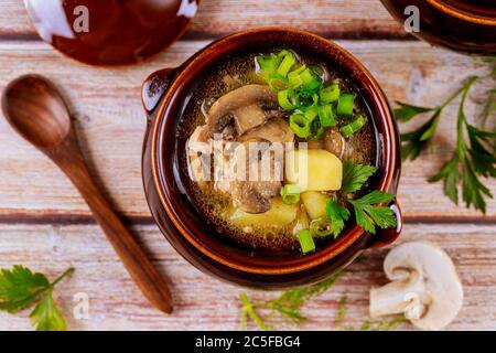 Suppe mit Kartoffeln, Pilzen und Fleisch in Tontopf mit Löffel. Stockfoto