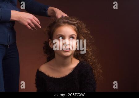 Studio-Portrait eines kleinen Mädchens, mit einem verärgerten Gesicht und lockigen lockigen Haaren, die Frauenmutter die Hände fixieren ihr Haar Stockfoto