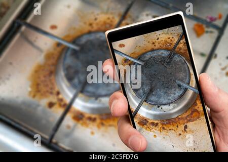 Alte schmutzige Gasherd auf Smartphone-Bildschirm. Reinigung von Haushaltsgeräten. Stockfoto