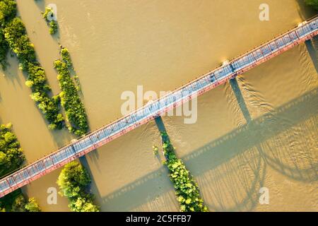 Luftaufnahme einer schmalen Straßenbrücke, die sich über einen schlammigen, breiten Fluss in grüner ländlicher Umgebung erstreckt. Stockfoto
