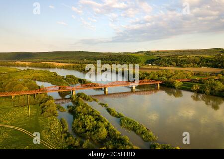Luftaufnahme einer schmalen Straßenbrücke, die sich über einen schlammigen, breiten Fluss in grüner ländlicher Umgebung erstreckt. Stockfoto