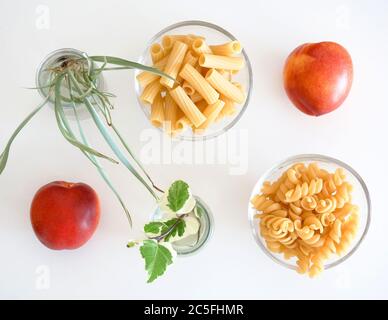 Rohe Pasta in winzigen Glasschalen, süße Nektarinen und Blumen vermengen Pflanzen auf weißem Hintergrund. Konzept für die Lebensmittelknollung Stockfoto