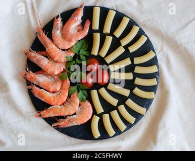 Gesunde Meeresfrüchte servieren rohe Zutaten auf schwarzem runden Granituntersetzer: Pasta, Tomaten, große Garnelen. Vegetarische Gerichte. Stockfoto