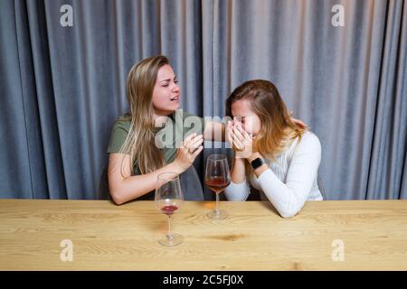 Eine Frau tröstet einen traurigen depressiven Freund, der Hilfe braucht. Depression mit Alkohol-Konzept. Verärgert junge Mädchen mit unglücklichen Gesicht hält ein Glas Wein lo Stockfoto