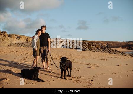 Millennial Paar am Strand mit zwei schwarzen Labradors stehen Stockfoto