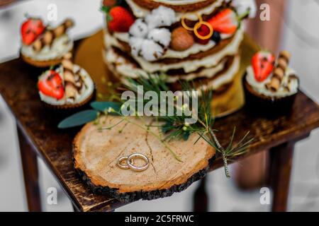 Hochzeitstorte mit Obst und einem alten Holztisch mit Nadeln von Kegeln und Blättern während einer Hochzeitszeremonie im Winter auf Schnee inmitten eines Waldes Stockfoto