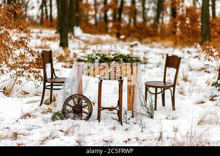 Hochzeit alter Holztisch mit Nadelspitze und Blattdekoration während der Hochzeitszeremonie im Winter auf Schnee mitten im Wald bedeckt mit frischem sno Stockfoto