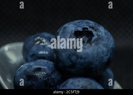 Blaubeeren Makro Nahaufnahme von übereinander überlagert und in einem Teelöffel vor einem dunklen Hintergrund gefliest. Stockfoto