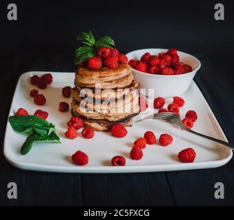 Schokoladen-Pfannkuchen mit frischen Himbeeren und Minze auf schwarzem Hintergrund Stockfoto