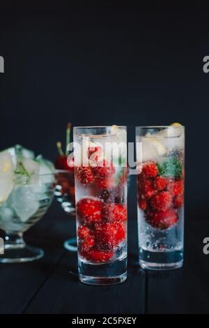 Kalte Limonade mit Himbeeren, Zitrone, Eis und Kirschen auf schwarzem Hintergrund Stockfoto