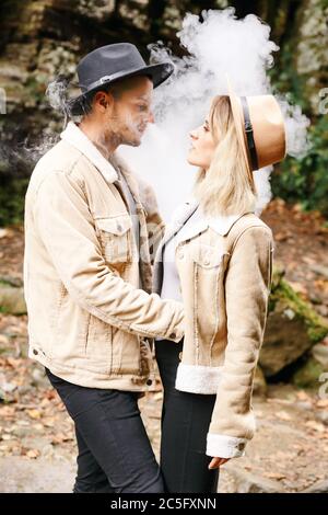 Paar in der Wolke. Zwei in Rauch. Touristen in kalten Herbstwald mit Vape. Mann und Frauen in Rauch. Zwei Raucher. Schönes Paar im Nebel. E-Zigarett Stockfoto