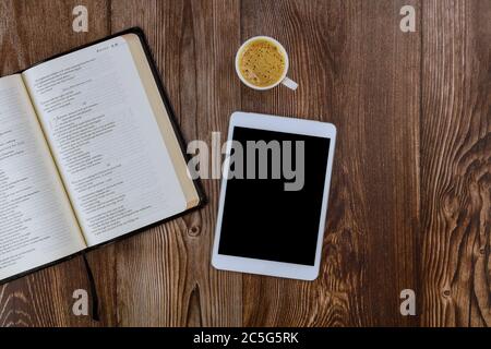 CHICAGO IL US 01 JULY 2020: Öffnen Sie die Heilige Bibel auf einem Holztisch liegend in einer Lesung der digitalen Tablette mit einer Tasse Kaffee Stockfoto