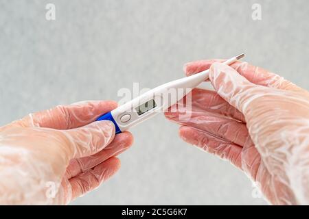 Weibliche Hände tragen in Vinylhandschuhen mit einem Digitalthermometer. Stockfoto