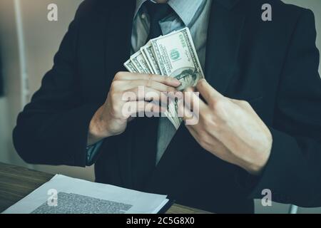 Geschäftsmann, der Stapel Geldscheine in seine Kleidertasche legt. Stockfoto