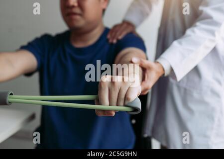 Asiatische männliche Physiotherapeut Abstieg Arbeit mit Patienten tun Stretching-Übung mit einem flexiblen Übungsband im Klinikraum. Stockfoto