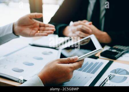 Manager verwenden ein Tablet und erklären dem Mitarbeiter im Bürozimmer den zusammenfassenden Bericht. Stockfoto