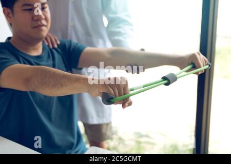 Asiatische männliche Physiotherapeut Abstieg Arbeit mit Patienten tun Stretching-Übung mit einem flexiblen Übungsband im Klinikraum. Stockfoto