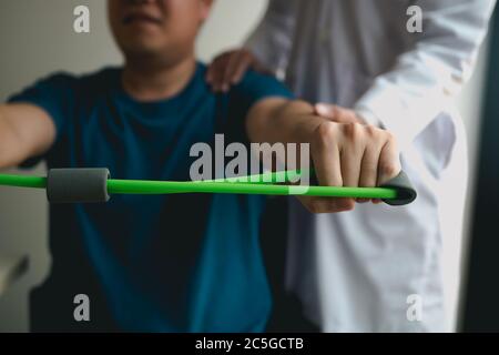 Asiatische männliche Physiotherapeut Abstieg Arbeit mit Patienten tun Stretching-Übung mit einem flexiblen Übungsband im Klinikraum. Stockfoto