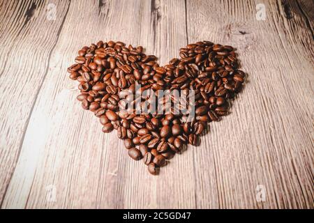 Eine Handvoll Kaffeebohnen in Form eines Herzens, Nahaufnahme. Geröstete herzförmige Kaffeebohnen auf dem Tisch, selektiver Fokus. Romantisches Thema. Stockfoto