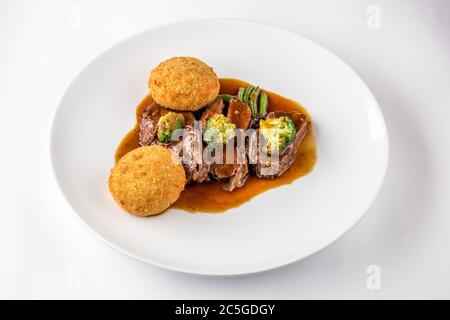Schweinebacken in Sauce mit Brokkoli und grünen Bohnen auf einem weißen Teller. Stockfoto