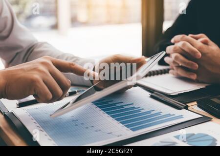 Manager verwenden ein Tablet und erklären dem Mitarbeiter im Bürozimmer den zusammenfassenden Bericht. Stockfoto