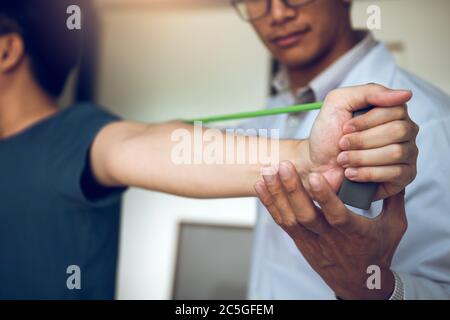 Asiatische männliche Physiotherapeut Abstieg Arbeit und helfen, die Hände von Patienten mit Patienten tun Stretching-Übung mit einem flexiblen exer zu schützen Stockfoto