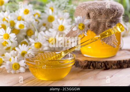 Süßer Frühlingshonig im Glas und kleine Glasschüssel mit einer Honigtaube. Komposition von aromatischem Honig auf dem Tisch mit frischen Kamillenblüten Stockfoto