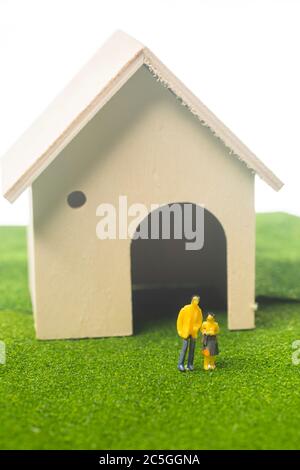 Miniatur-Paar-Figuren vor einem Spielzeughaus, Kauf oder Besitz eines Hauses Konzept Stockfoto