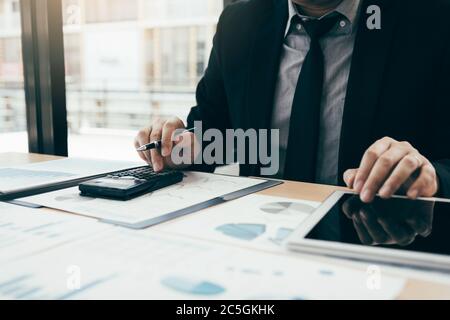 Geschäftsleute verwenden Rechner, um den Unternehmensgewinn zu berechnen, indem sie von den Ausgaben abziehen und mit Tablets Informationen auf Tabelle in der finden Stockfoto