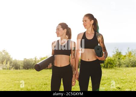 Zwei Damen in schwarzen sportlichen Tops und Leggings stehen und träumen zusammen zur Seite Stockfoto