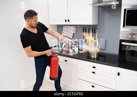 Mann mit Feuerlöscher zu stoppen Feuer zum Brennen von kochenden Topf in der Küche Stockfoto