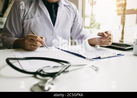 Arzt Hand halten Stift schreiben Patientenliste auf Notizblock und sprechen mit dem Patienten über Medikamente und Behandlung. Stockfoto
