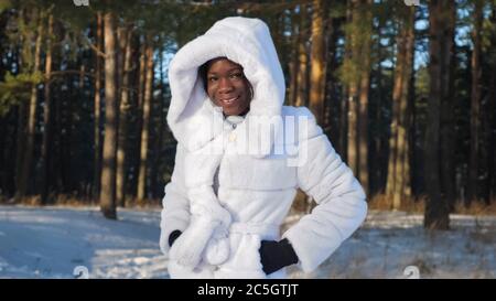 Lächelndes afroamerikanisches Mädchen in weißem Pelzmantel kleidet Kapuze im Winter Park Nahaufnahme Stockfoto