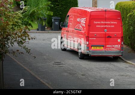 Ein roter Parcel Force-Van parkte auf einer Straße, während der Fahrer ein Paket abliefert. Stockfoto