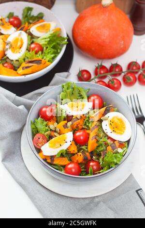Gemüsesalat mit gegrillter Karotte, Kirschtomaten, Kürbis, Salat, gekochten Eiern und Sesamsamen. Stockfoto